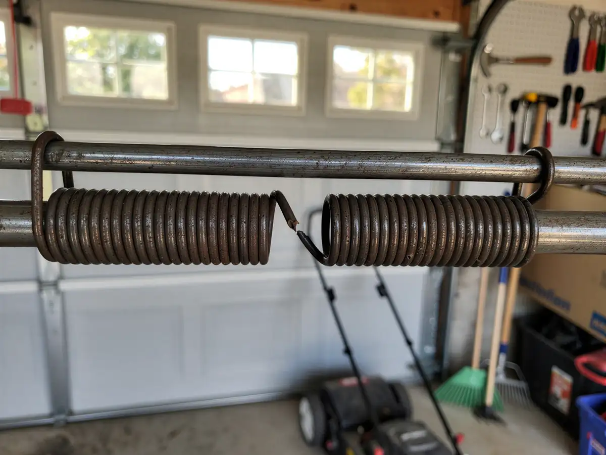 A rusted, broken torsion spring is on a metal rod in a garage.